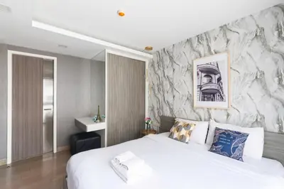 a bedroom with a white bed and a stone wall at Dazzle Sukhumvit 7 by LeFoyer in Bangkok