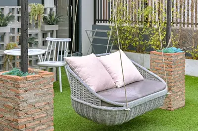 a wicker swing chair with a pillow on a patio at Shewin de Bangkok in Ban Bang Bamru