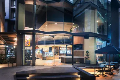 a large glass building with tables and chairs outside at Lumen Bangkok Udomsuk Station in Bangkok