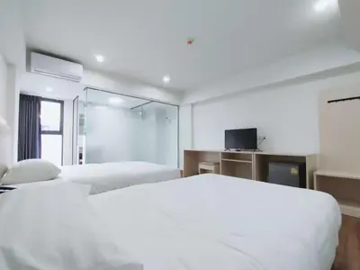 a white bedroom with two beds and a tv at Lucky Elephant Hotel in Ban Bang Toei (1)