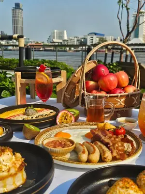 a table with plates of food and a basket of fruit at Ten Six Hundred, Chao Phraya, Bangkok by Preference, managed by The Ascott Limited in Bangkok