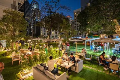 a group of people sitting at tables in a garden at night at Floral Court Hotel & Residence Sukhumvit 13 in Bangkok