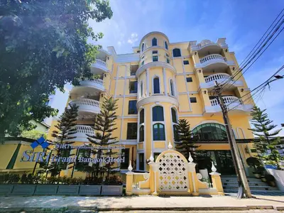 a large yellow and white building with trees in front of it at Siri Ratchadamnoen Bangkok Hotel in Bangkok