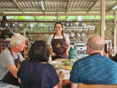 a group of people standing around a woman in a kitchen at The Thai House Homestay & Thai Cooking Experiences in Ban Bang Sano