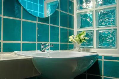 a blue tiled bathroom with a sink and a vase of flowers at Alley & Pier in Bangkok