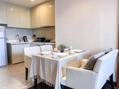 a dining room table with white chairs and a kitchen at Grand Modern 2BR - Ultra Fast WiFi - Phrom Phong in Bangkok
