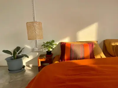 a bedroom with an orange bed and a potted plant at Baan KhaoSoi - Private room in a rooftop hostel 3rd floor in Khlong San