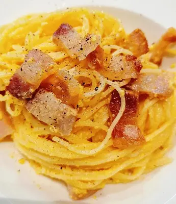 a white plate of pasta with bacon and cheese at COZY Bangkok BM B&B in Amphoe Phra Khanong