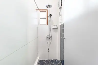 a shower in a white bathroom with black tiles at Sathorn Private Pool Villa in Bangkok