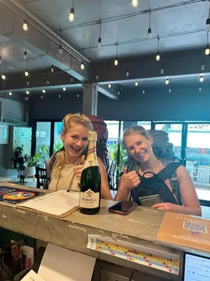 two women sitting at a bar with a bottle of wine at Ti Thong Hostel in Bangkok