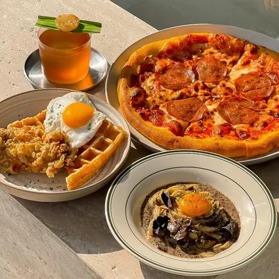 a table with three plates of food and a pizza at Saan Hotel Sathorn in Bangkok