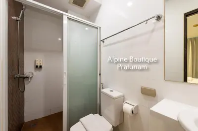 a bathroom with a toilet and a glass shower door at Alpine Boutique Pratunam in Bangkok