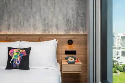 a bed with a pillow and a clock next to a window at Moxy Bangkok Ratchaprasong by Marriott in Bangkok