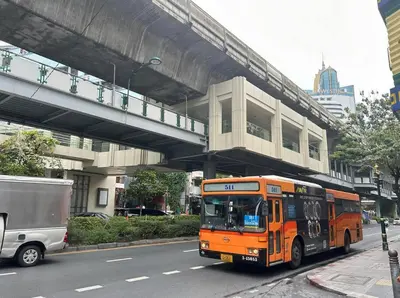 an orange bus driving down a street under a bridge at Sukhumwit Soi 10 at VENiO in Khlong Toei