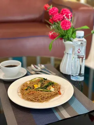 a plate of spaghetti on a table with a vase of flowers at Grand Tower Inn Sathorn Hotel in Bangkok