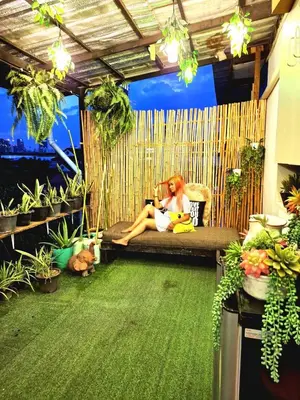 a woman sitting on a couch in a room with plants at EZ Sleep @ Ratchada 19 in Bangkok