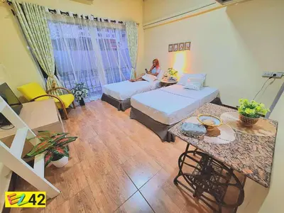 a room with two beds and a woman sitting on a couch at EZ Sleep @ Ratchada 19 in Bangkok