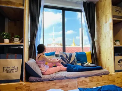 a woman sitting on a bed looking out a window at Private house with Pagoda view, near Grand Palace in Bangkok