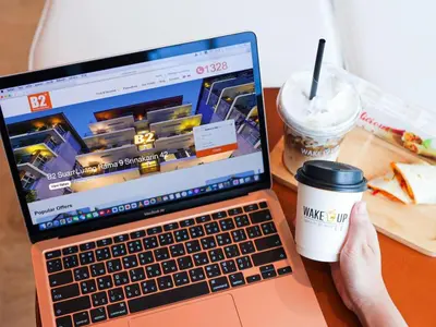 a person sitting at a desk with a laptop and a cup of coffee at B2 Suan Luang Rama 9 Srinakarin 42 Boutique & Budget Hotel in Bangkok