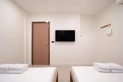 two beds in a room with a television on the wall at Townhouse in Pratunam Bangkok in Bangkok