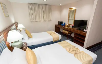 a hotel room with two beds and a desk and a television at The Grand Sathorn in Bangkok