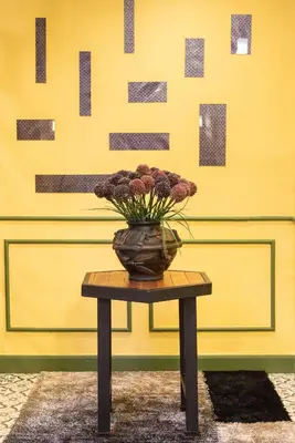 a vase on a table in front of a yellow wall at 75 Paradise Lane Managed by Loft Group in Bangkok