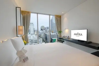 a bedroom with a white bed and a large window at Amara Bangkok Hotel in Bangkok