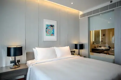 a bedroom with a large white bed and a bathroom at Amara Bangkok Hotel in Bangkok