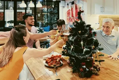 a group of people drinking wine around a table with a christmas tree at Single Beds, Private Bath & Balcony, Shared Kitchen with Local Family by Pillows & Purrs in Bangkok