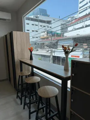 a kitchen with a table and stools and a large window at First Villa Life Hostel in Bangkok
