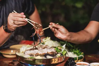 two people eating food with chopsticks on a table at Baanrongmai Canal Front Homestay in Bang Chak