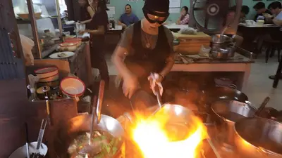 a man cooking food over a fire in a kitchen at xx GO INN The Grand Palace โกอินน์ MRT สามยอด in Bangkok