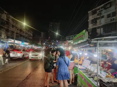 a group of people standing around a food stand on a city street at \u8f89\u714c\u591c\u5e02 4\u623f\u6cf3\u6c60\u82b1\u56ed\u522b\u5885 \u8ba24\u65e5\u63d0\u4f9b\u514d\u8d39\u63a5\u673a\u4e00\u6b21 in Bangkok
