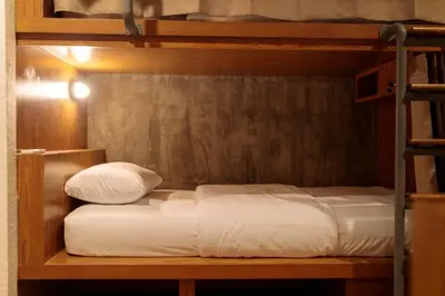 a bunk bed with white sheets and pillows on it at Rere Hostel - รีรีโฮสเทล in Bangkok