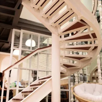 a white spiral staircase in a room with a table at Rere Hostel - รีรีโฮสเทล in Bangkok