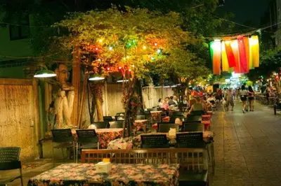 a restaurant with tables and people walking down a street at night at The Street Hostel Bangkok in Bangkok