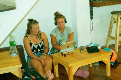 two women sitting next to a table with a laptop at The Street Hostel Bangkok in Bangkok