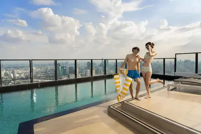 a man and a woman standing on the edge of a swimming pool at Cassia Rama 9 Bangkok, part of Banyan Group in Bangkok