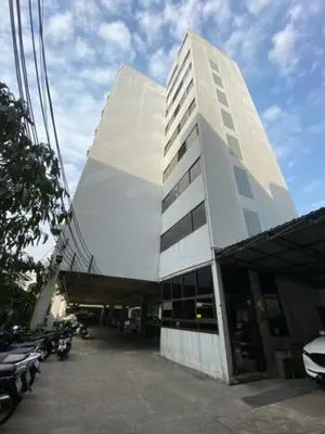 a tall white building with cars parked in a parking lot at รัตนากร แมนชั่น in Bang Su