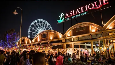 a crowd of people standing outside of a building with a ferris wheel at XX GO INN Asiatique BKK Charoen krung- โกอินน์ เอเซียทีค เจริญกรุง in Godown