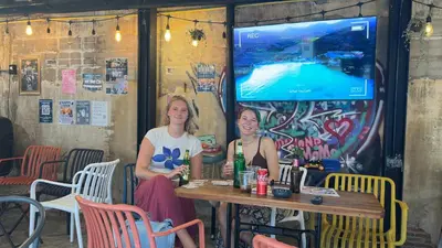 two women sitting at a table in front of a screen at AREA81 HIDEOUT Hostel Khaosan in Bangkok