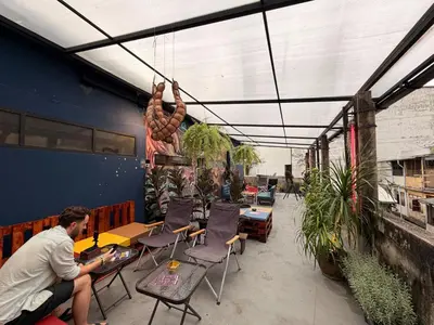 a man sitting at a table in a patio with plants at AREA81 HIDEOUT Hostel Khaosan in Bangkok