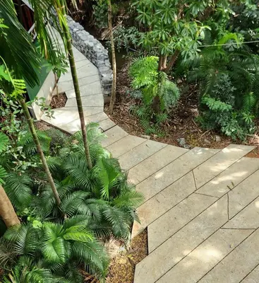 a wooden walkway through a garden with palm trees at Hiddenwoods in Bang Chak
