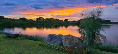 a sunset over a lake with a bench and a rock at Tiny Island Lake Lodge in Bangkok