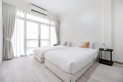 a white bedroom with two beds and a window at Haus Ekkamai 2 in Khlong Toei