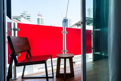a chair and stool on a balcony with a red wall at Elite Hotel Asok Sukhumvit 20 in Bangkok