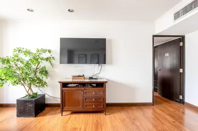 a room with a tv on a wall with a wooden table at Artichoke Suite Sukhumvit, Nana BTS in Bangkok