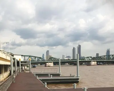 a dock with benches and a bridge over the water at Seen Hostel Bangkok The Riverwalk in Bangkok