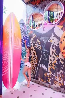 a woman standing in front of a mural with her surfboard at \u8fea\u5965\u82b1\u56ed\u66fc\u8c37\u661f\u7a7a\u6cf3\u6c60\u82b1\u56ed\u6d3e\u5bf9\u522b\u5885 in Bangkok