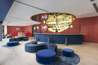 a lobby with blue stools and a red wall at Riva Vibe Hotel Bangkok by PCL in Bangkok